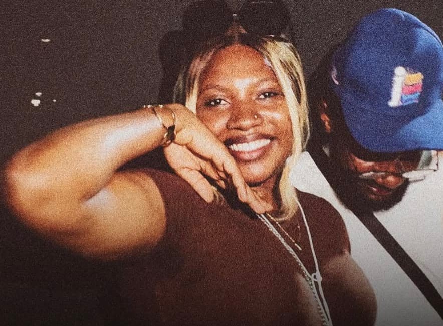 A smiling guest with her arm raised, posing beside a friend in a blue cap